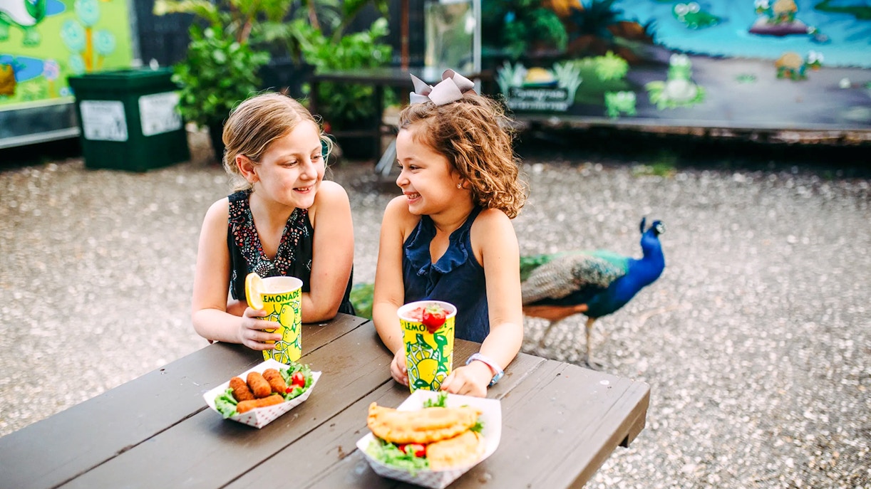 Kids enjoying a meal at Sawgrass Recreation Park with a peacock in the background.