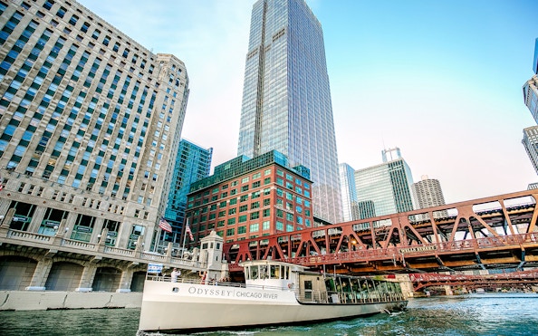 Boat "Odyssey Chicago River" cruising on Chicago River with skyscrapers and bridge.