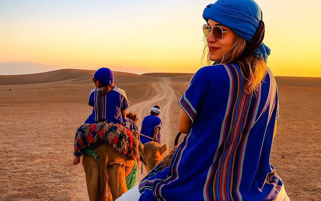 Camel ride in Agafay Desert, Marrakech at sunset with people in traditional attire.