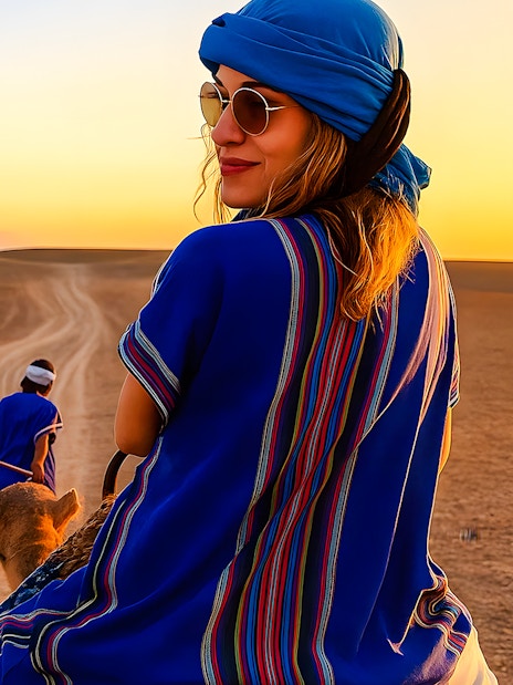 Camel ride in Agafay Desert, Marrakech at sunset with people in traditional attire.