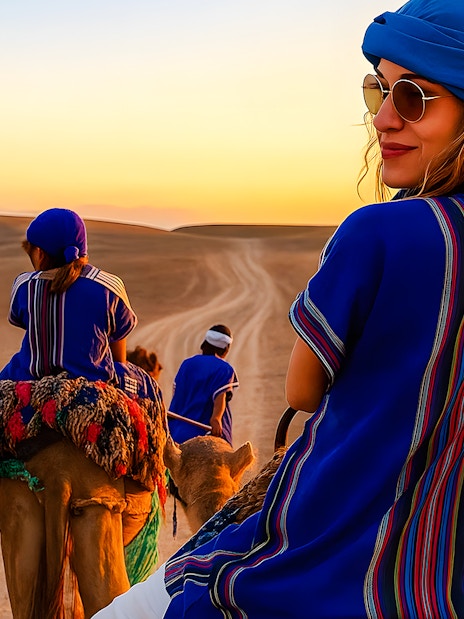 Camel ride in Agafay Desert, Marrakech at sunset with people in traditional attire.