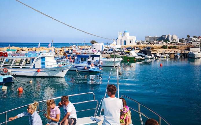 Boats docked at Protaras harbor with a view of a white chapel, part of the Blue Lagoon Cruise.