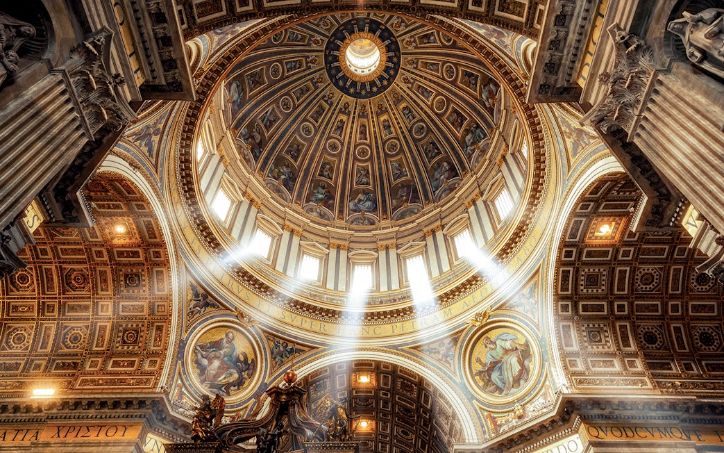 Dome and ornate ceiling of St. Peter’s Basilica with sunlight streaming through windows.