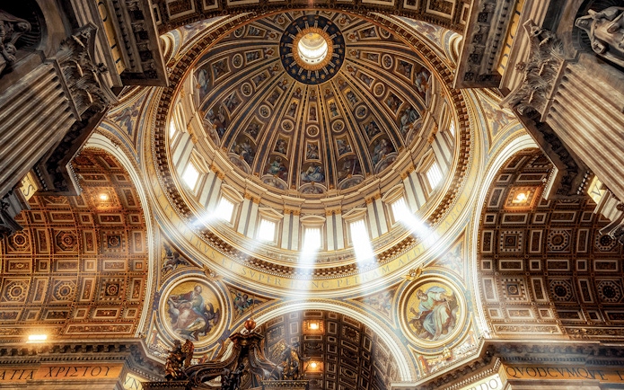 Dome and ornate ceiling of St. Peter’s Basilica with sunlight streaming through windows.