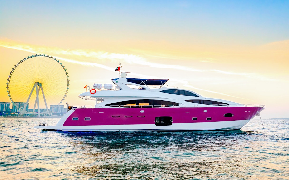 Yacht sailing at sunset near a large Ferris wheel in Dubai.