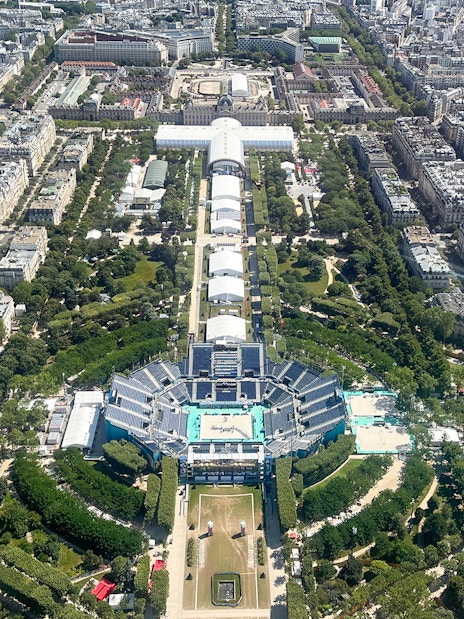 Aerial view of Paris cityscape with gardens and buildings, seen from the Eiffel Tower.