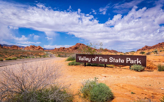 Valley of Fire State Park entrance sign with desert landscape and road in Nevada.