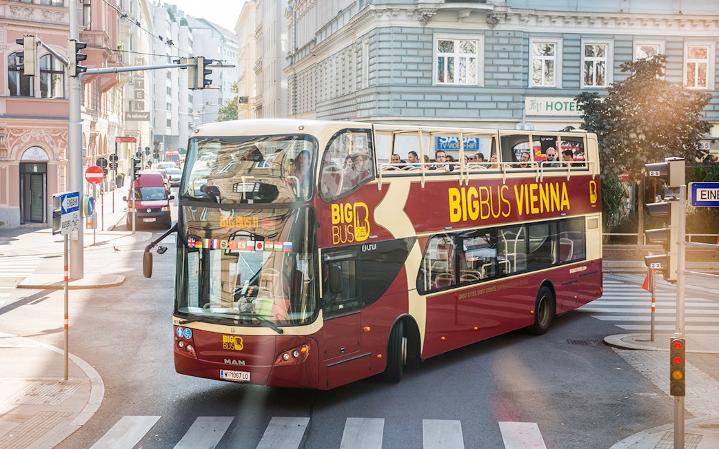 Vienna HopOn HopOff bus on city street with tourists on upper deck.