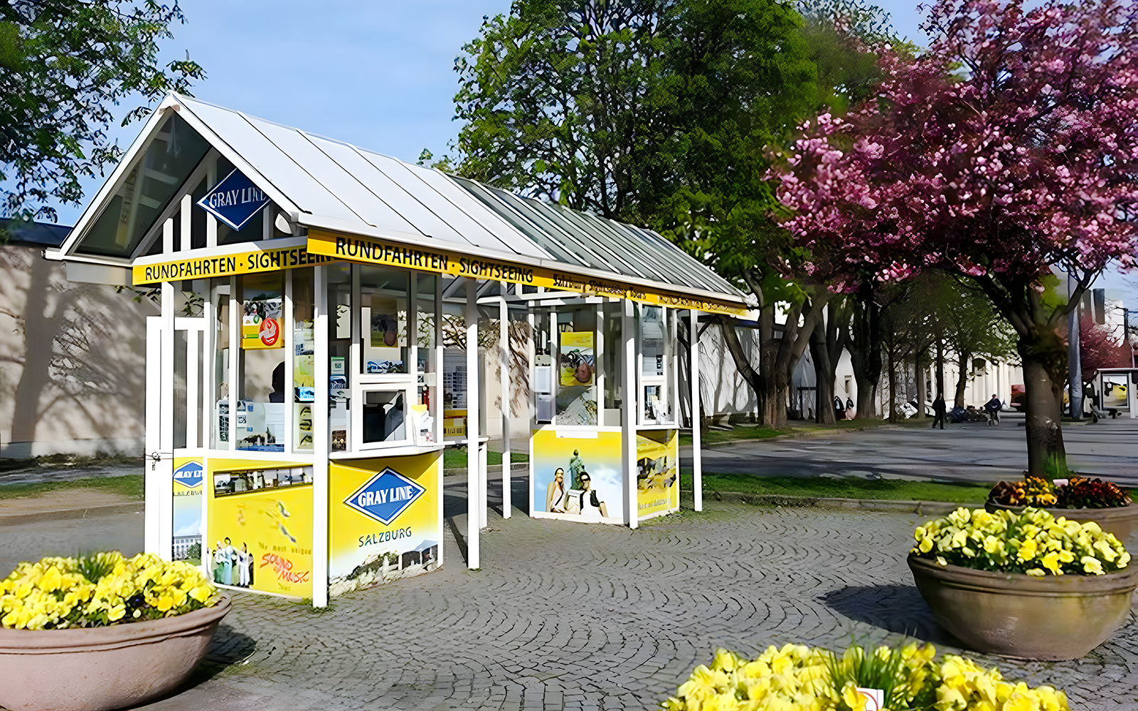 Salzburg hop-on hop-off tour ticket booth surrounded by trees and flowers.