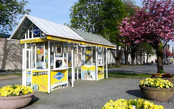 Salzburg hop-on hop-off tour ticket booth surrounded by trees and flowers.