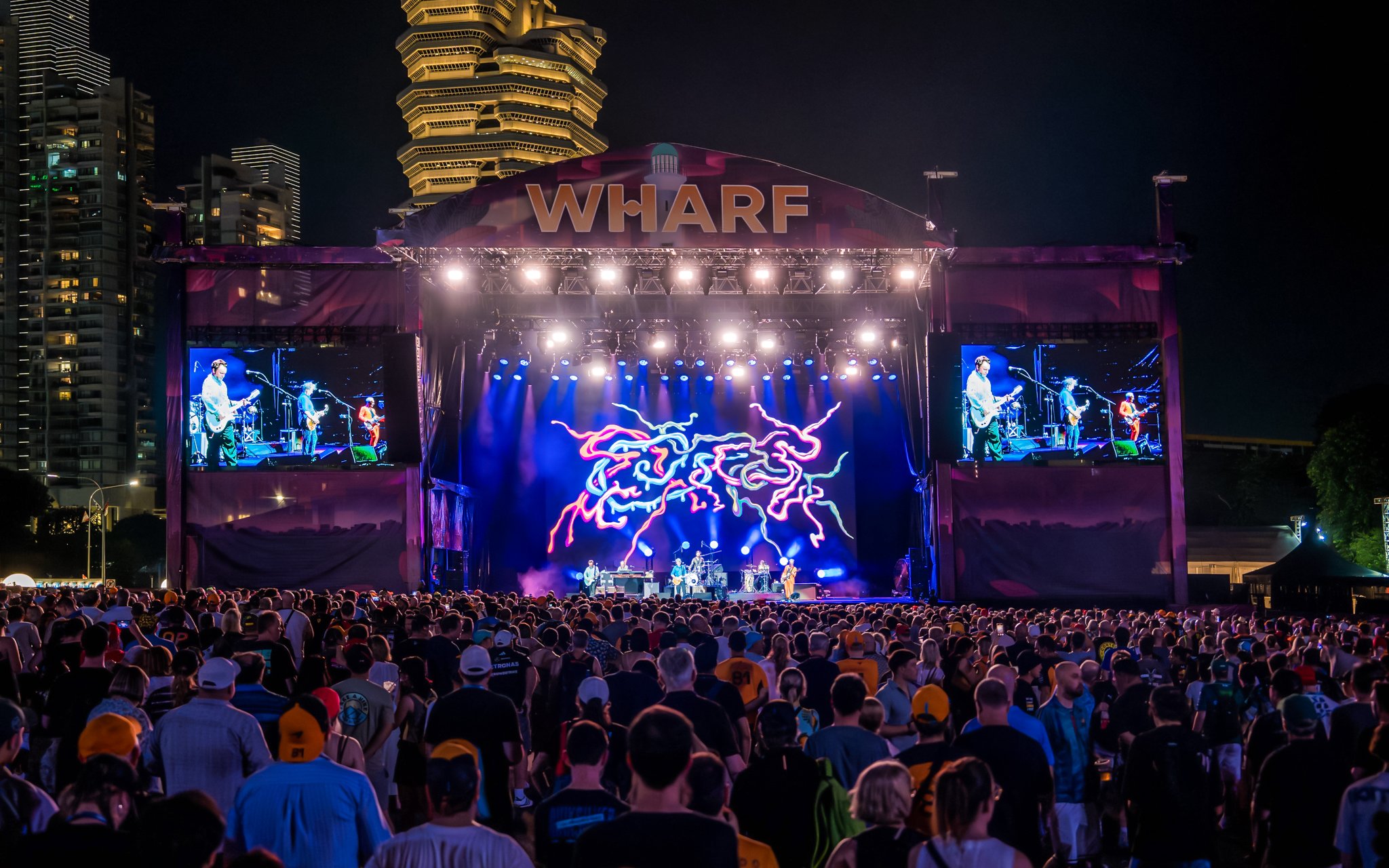 Crowd enjoying a concert at Wharf Stage with vibrant light display.