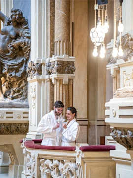 Couple enjoying drinks at QC Terme San Pellegrino spa, Italy, surrounded by ornate architecture.