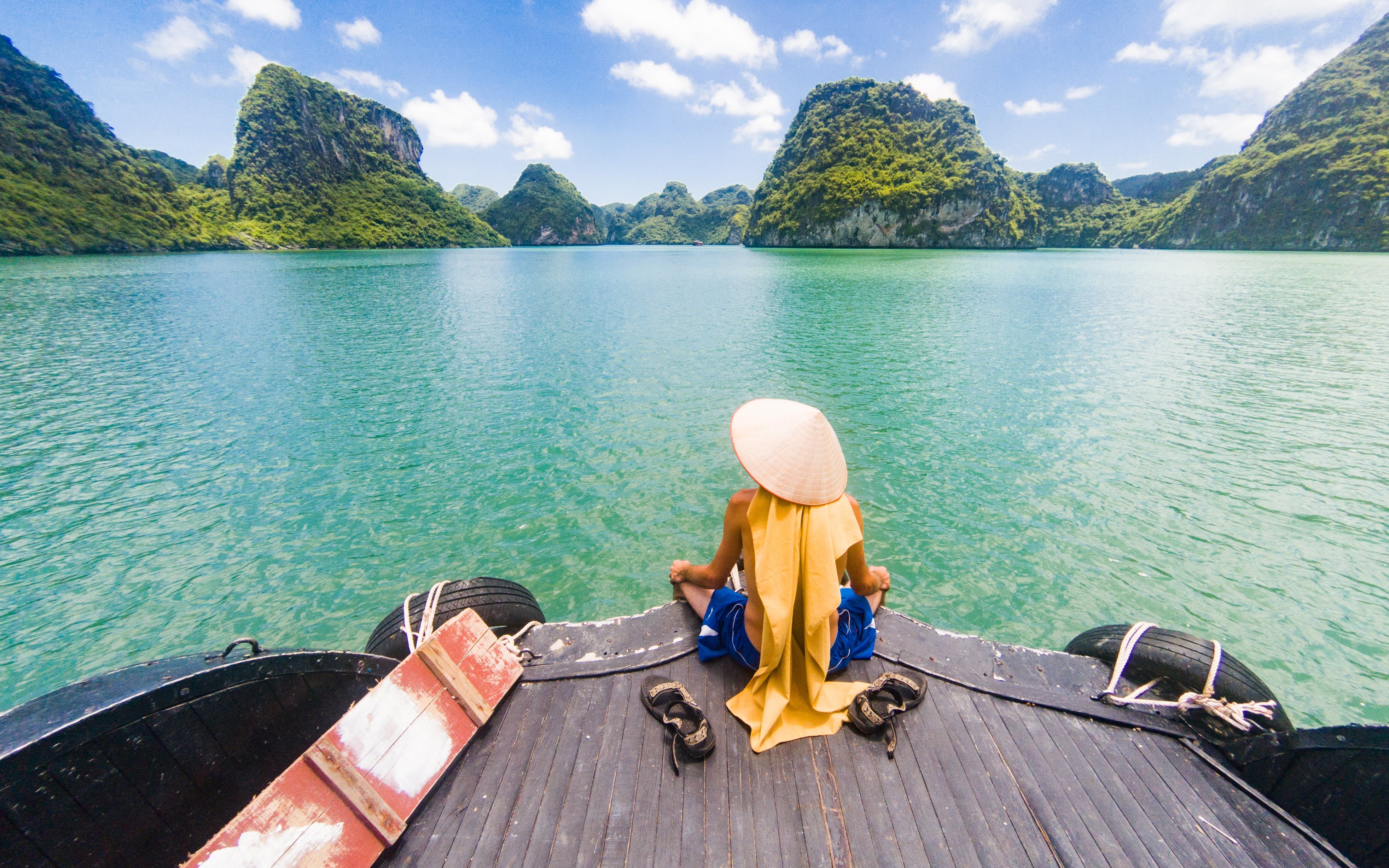 Man in Vietnamese hat on boat admiring Ha Long Bay limestone formations, Vietnam.