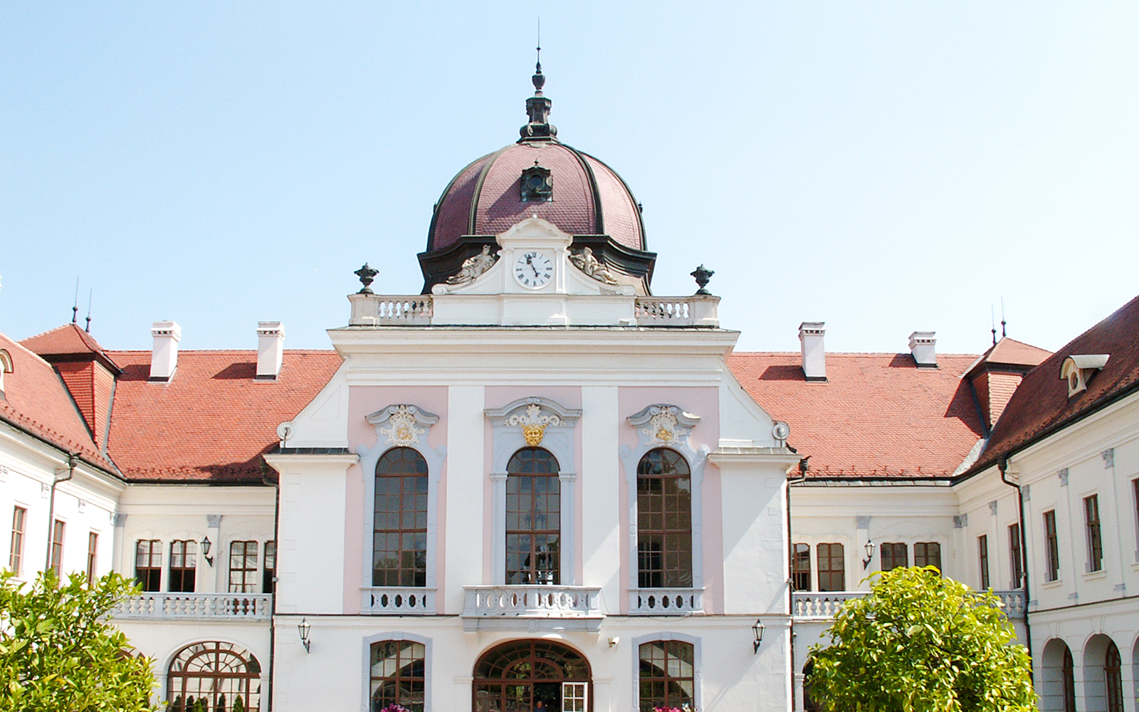 Exterior view of Royal Palace of Gödöllő with clock tower and red roof.