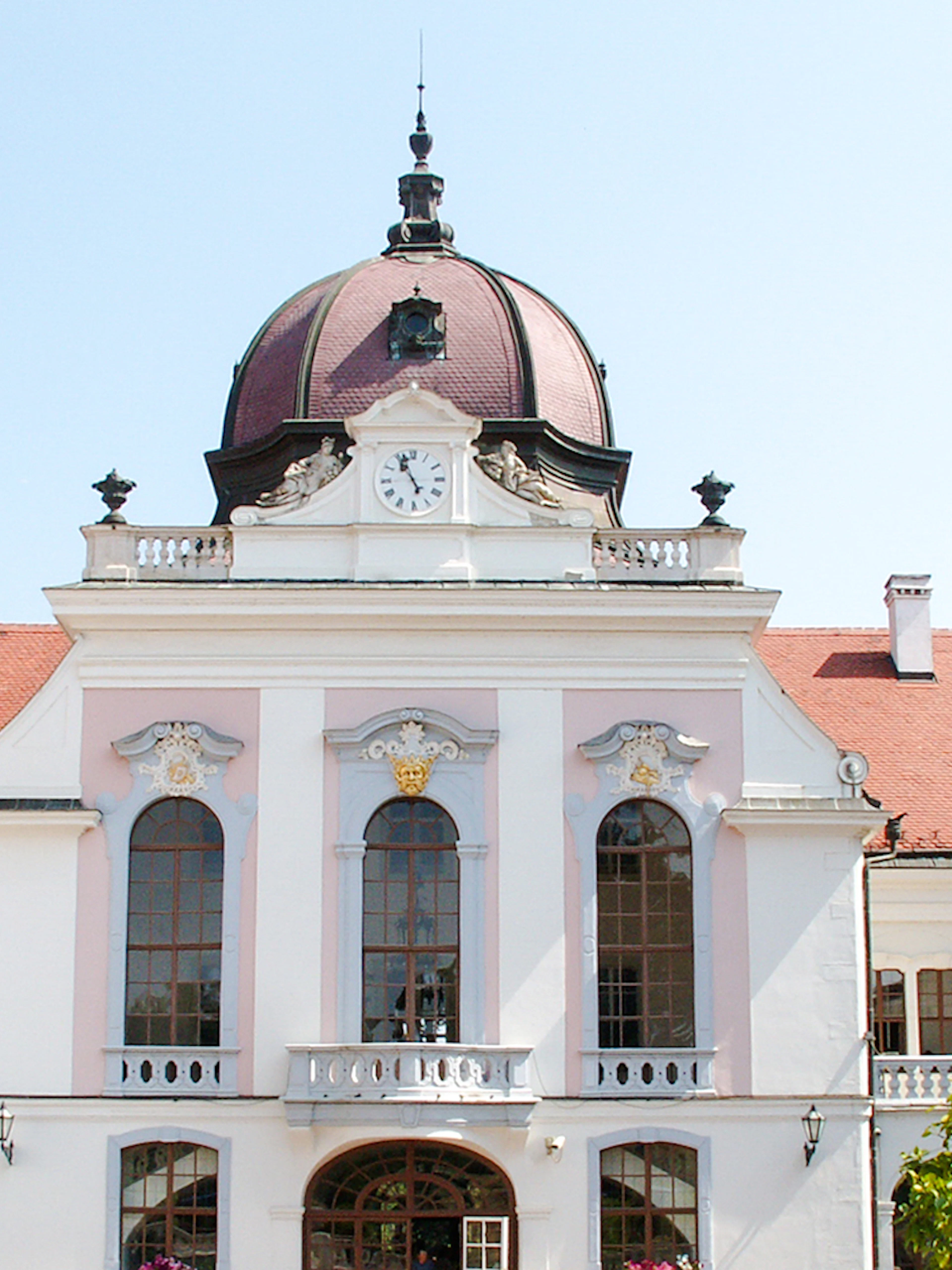 Exterior view of Royal Palace of Gödöllő with clock tower and red roof.