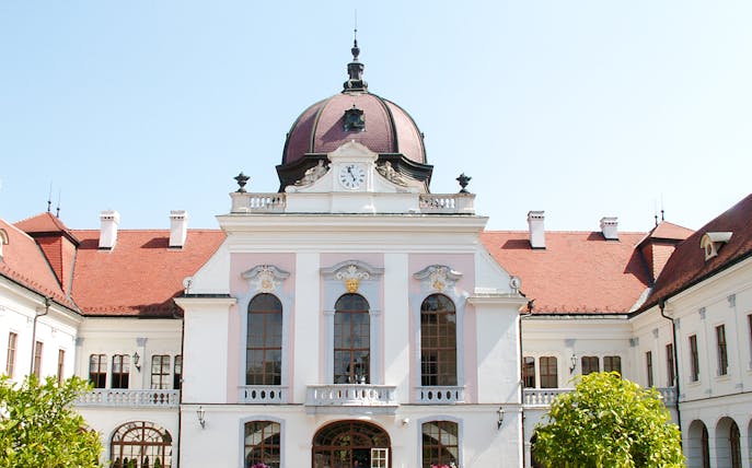 Exterior view of Royal Palace of Gödöllő with clock tower and red roof.
