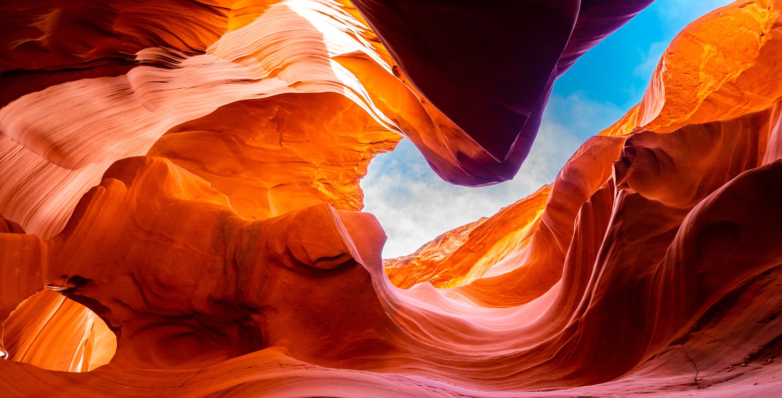 Lower Antelope Canyon's swirling red rock formations under a blue sky.