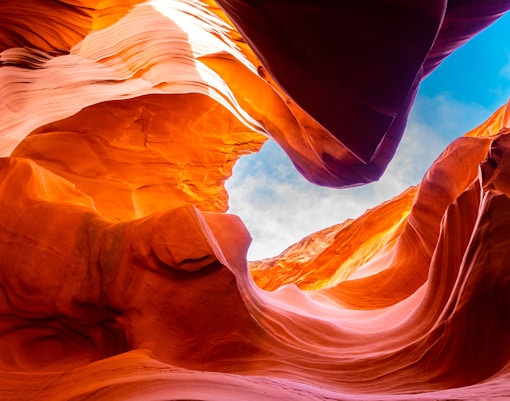 Lower Antelope Canyon's swirling red rock formations under a blue sky.