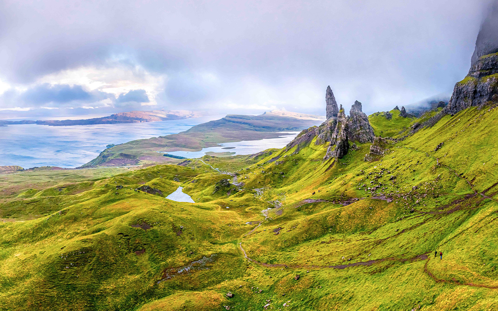 Loch Ness with lush green hills and rocky formations under a cloudy sky.