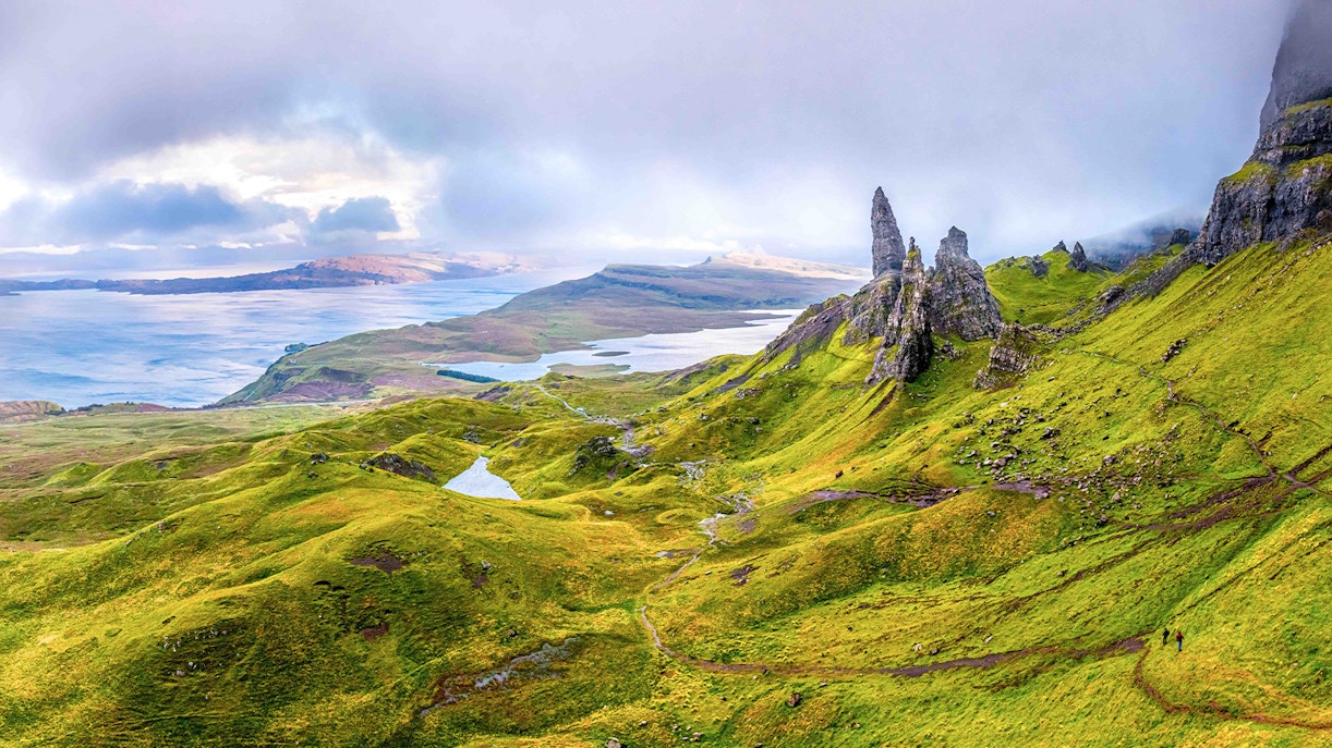 Loch Ness with lush green hills and rocky formations under a cloudy sky.