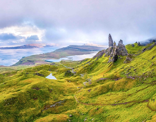 Loch Ness with lush green hills and rocky formations under a cloudy sky.