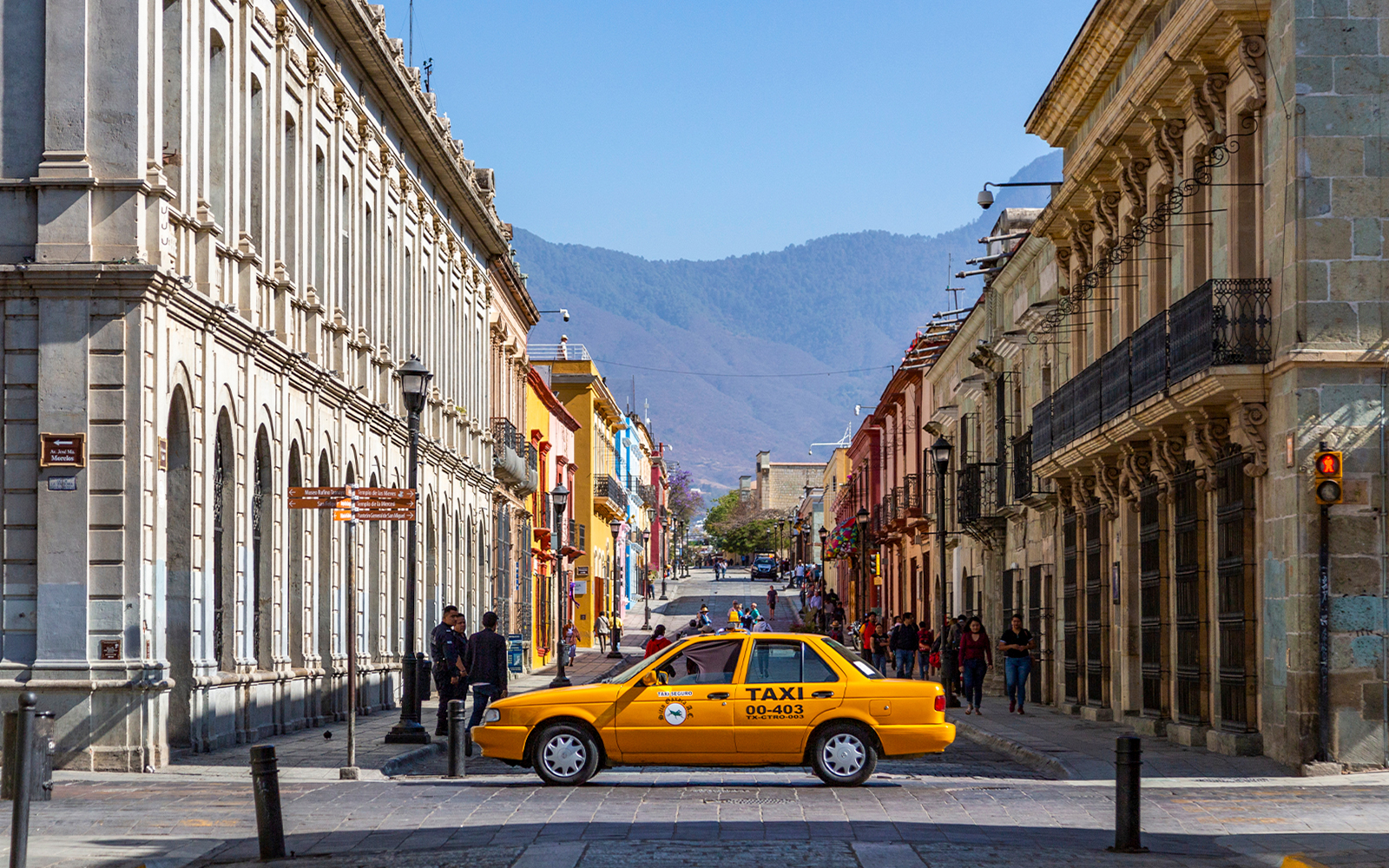 Yellow taxi driving on a street in Mexico City with historic buildings in the background.
