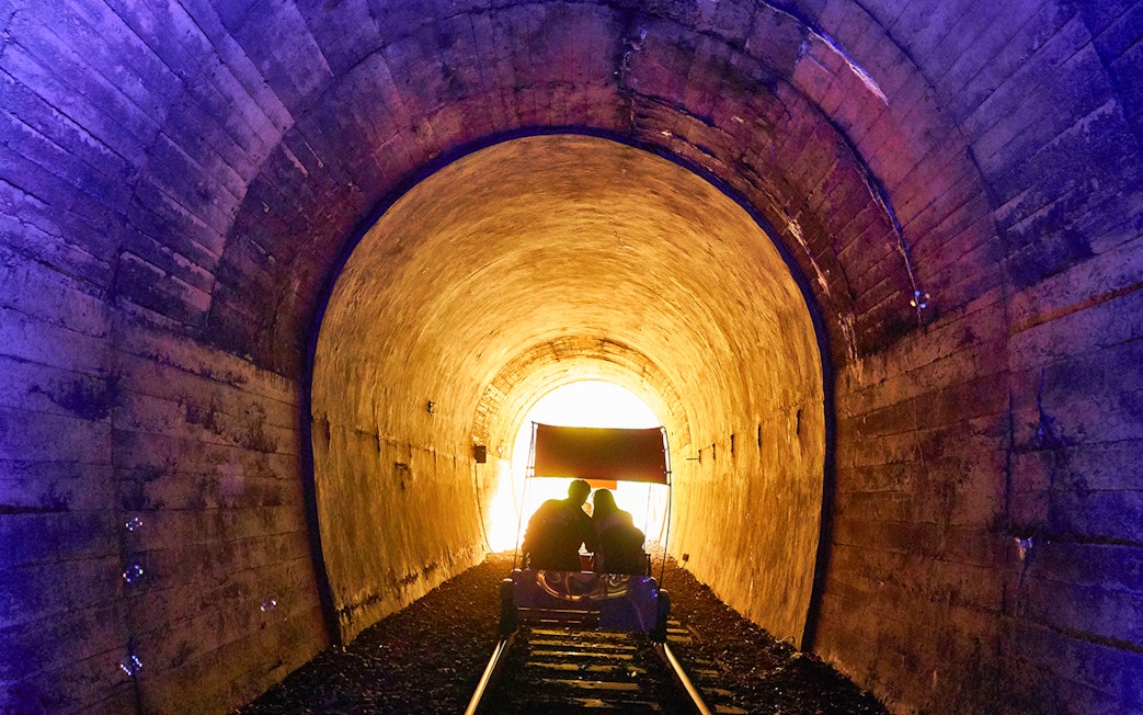 Couple on rail bike in illuminated tunnel, scenic track, South Korea.