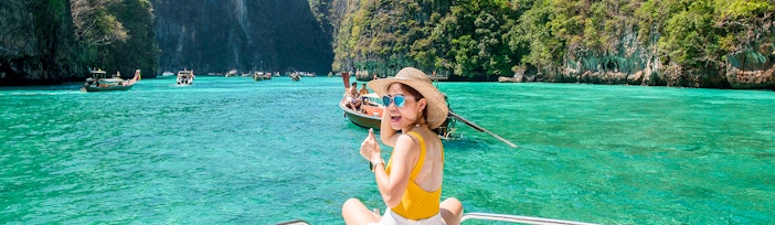 Woman on speedboat in turquoise waters of Phi Phi Island, surrounded by cliffs.