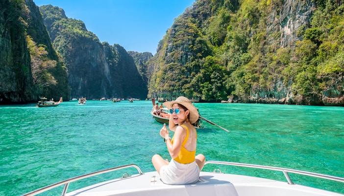 Woman on speedboat in turquoise waters of Phi Phi Island, surrounded by cliffs.