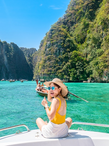 Woman on speedboat in turquoise waters of Phi Phi Island, surrounded by cliffs.