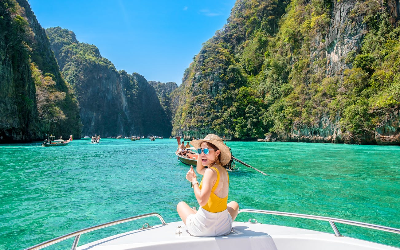 Woman on speedboat in turquoise waters of Phi Phi Island, surrounded by cliffs.