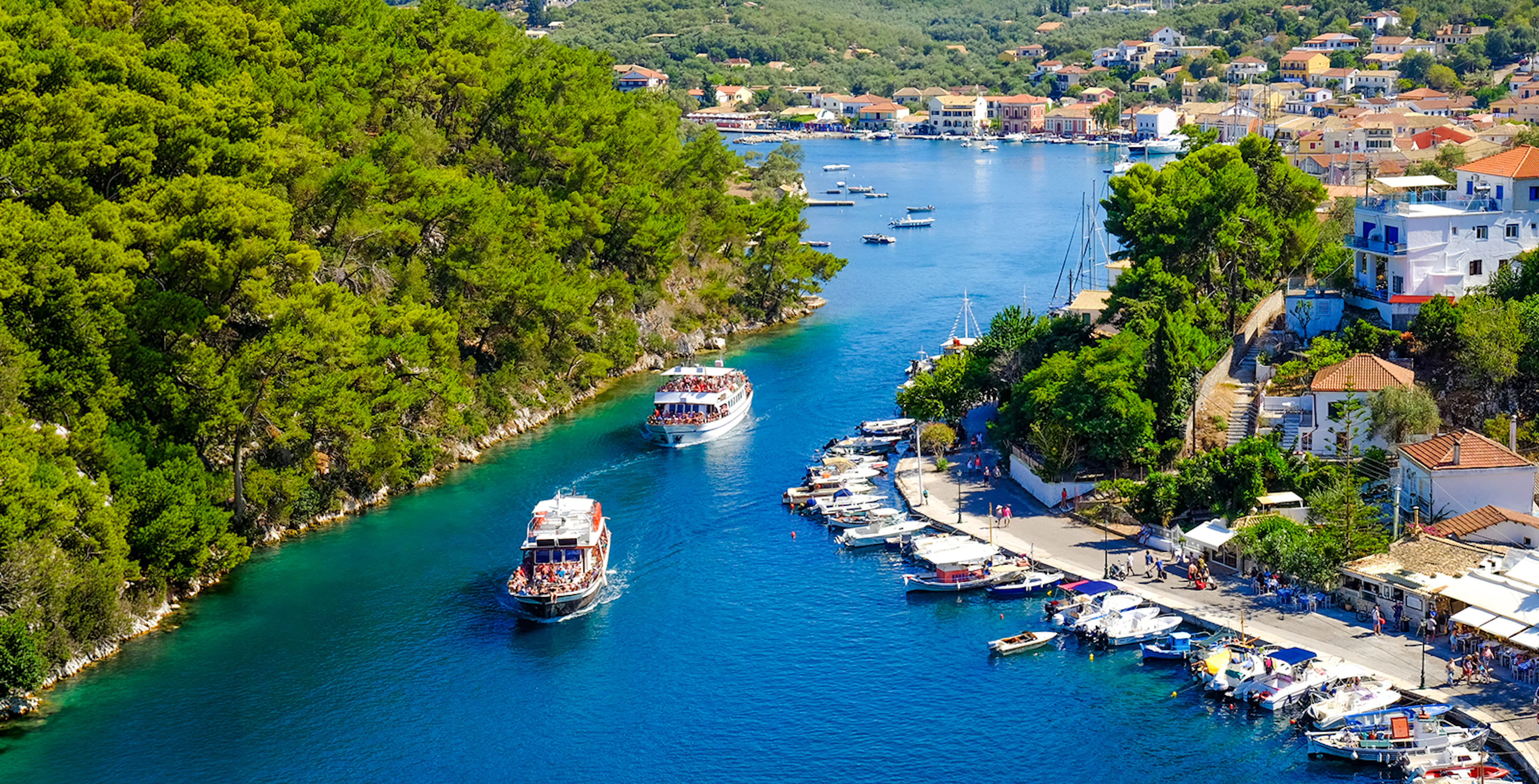 Boat entering the canal on Paxos Island, surrounded by lush greenery and coastal village, Corfu.