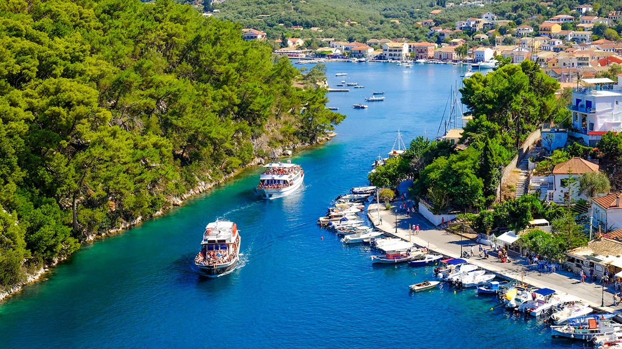 Boat entering the canal on Paxos Island, surrounded by lush greenery and coastal village, Corfu.