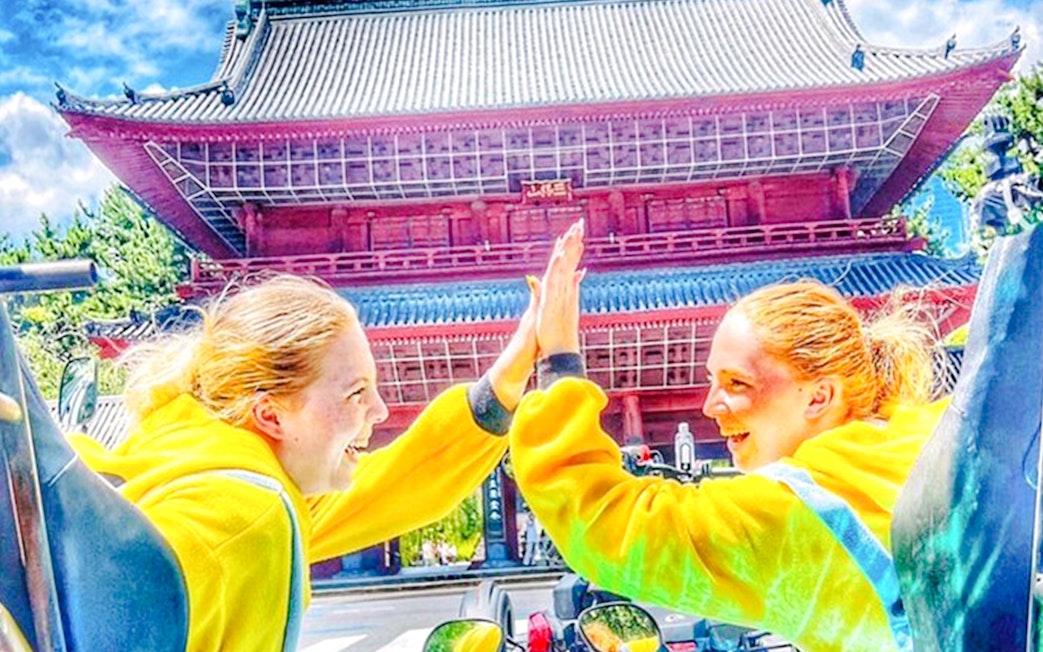 Two people in yellow costumes high-five in front of a Japanese temple.