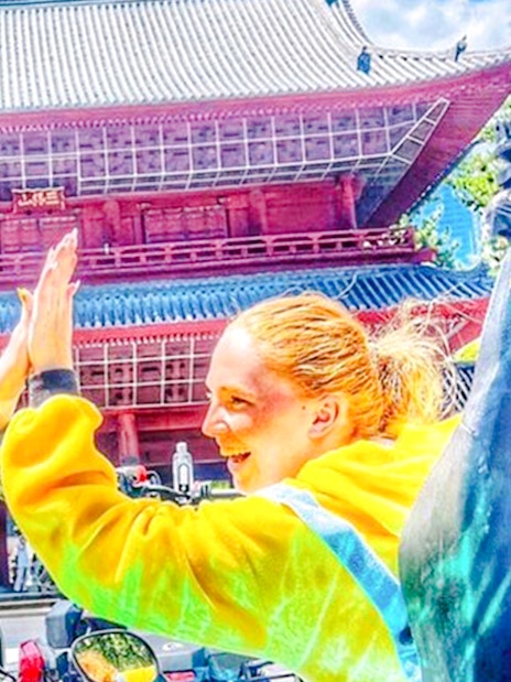 Two people in yellow costumes high-five in front of a Japanese temple.