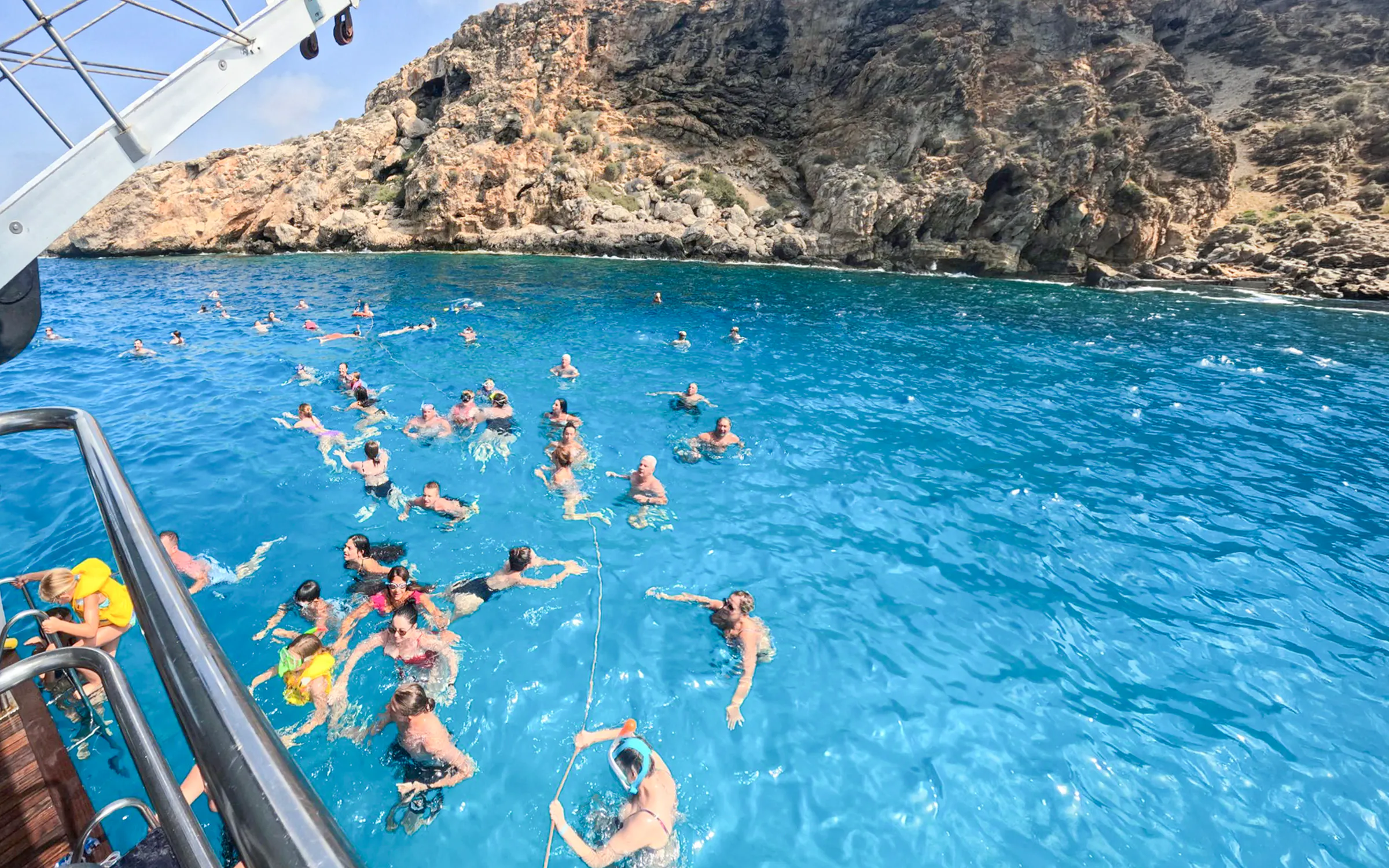 People swimming in the Blue Lagoon near rocky cliffs during a cruise from Larnaca.