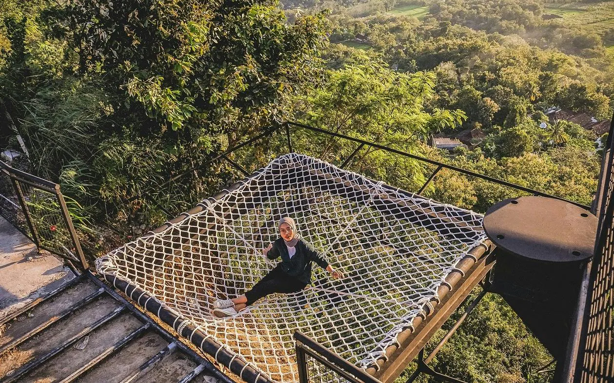 Person relaxing on a net platform overlooking lush greenery in Dubai.