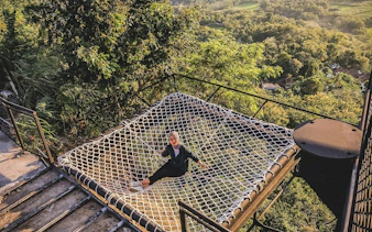 Person relaxing on a net platform overlooking lush greenery in Dubai.