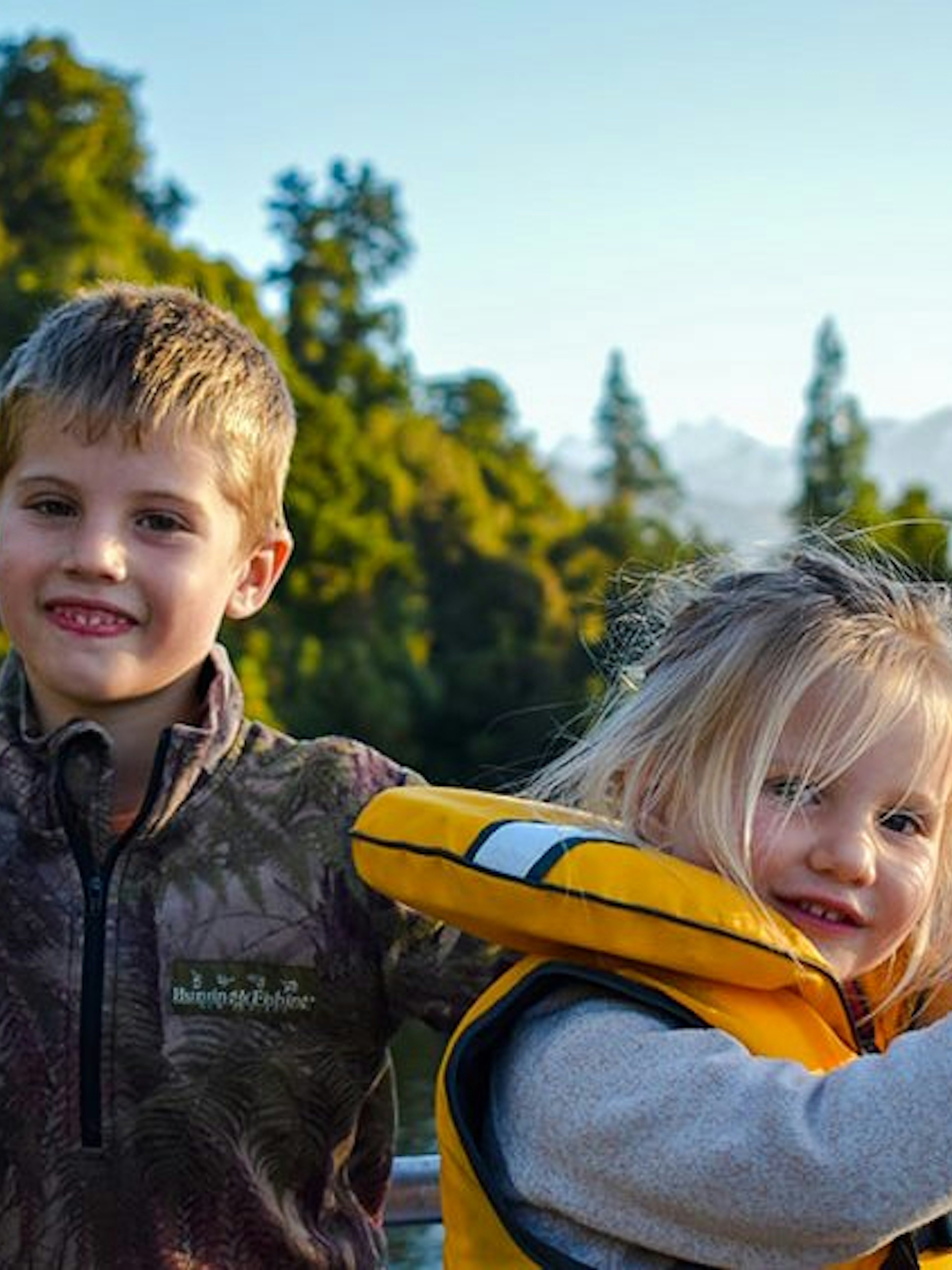 Children enjoying a scenic cruise on Lake Mapourika with forested hills in the background.