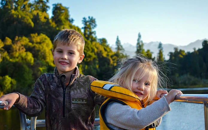 Children enjoying a scenic cruise on Lake Mapourika with forested hills in the background.