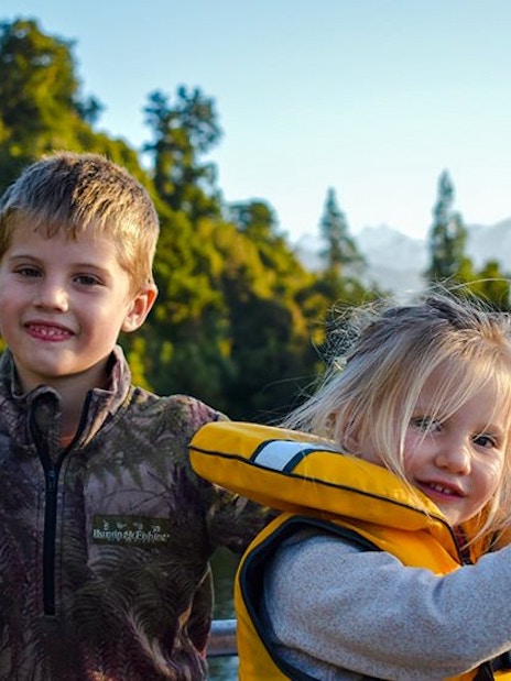 Children enjoying a scenic cruise on Lake Mapourika with forested hills in the background.