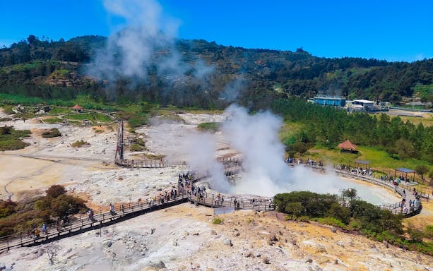 Tourists exploring the geothermal area in Dieng Plateau, Indonesia, with steam rising from the ground.