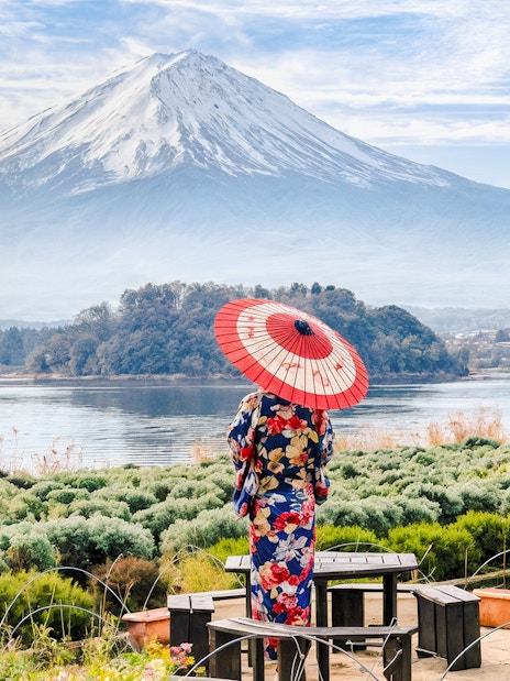 Woman in kimono with umbrella viewing Mount Fuji across a lake in Japan.