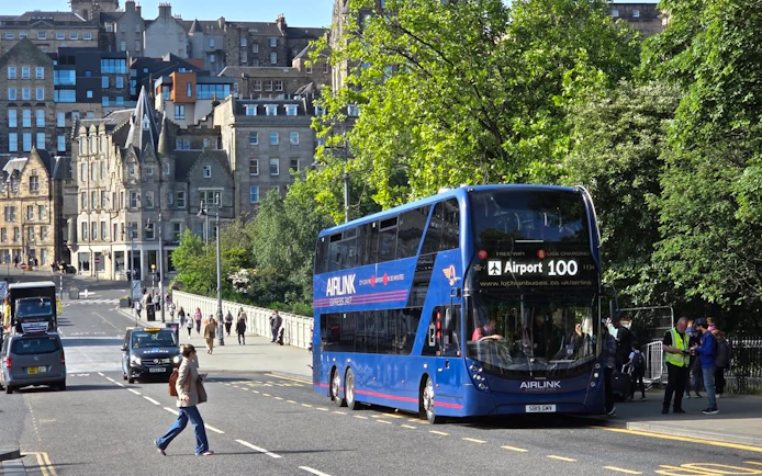 Edinburgh Airlink bus on city street with historic buildings in background.