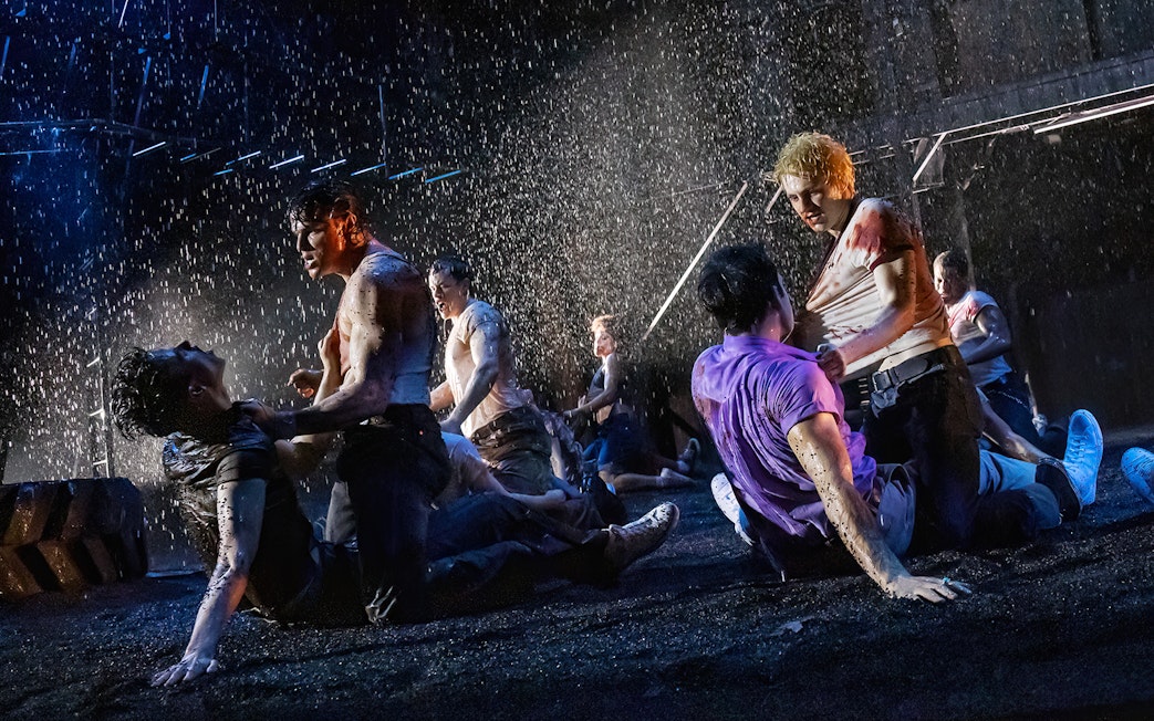 Men fighting in a dramatic rain-soaked scene from "The Outsiders" stage production.