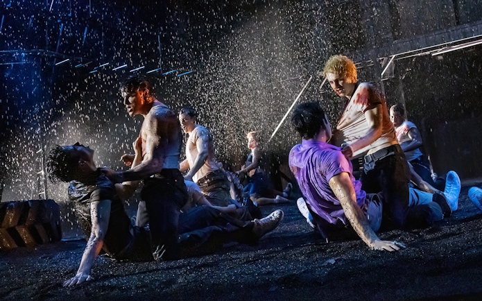 Men fighting in a dramatic rain-soaked scene from "The Outsiders" stage production.