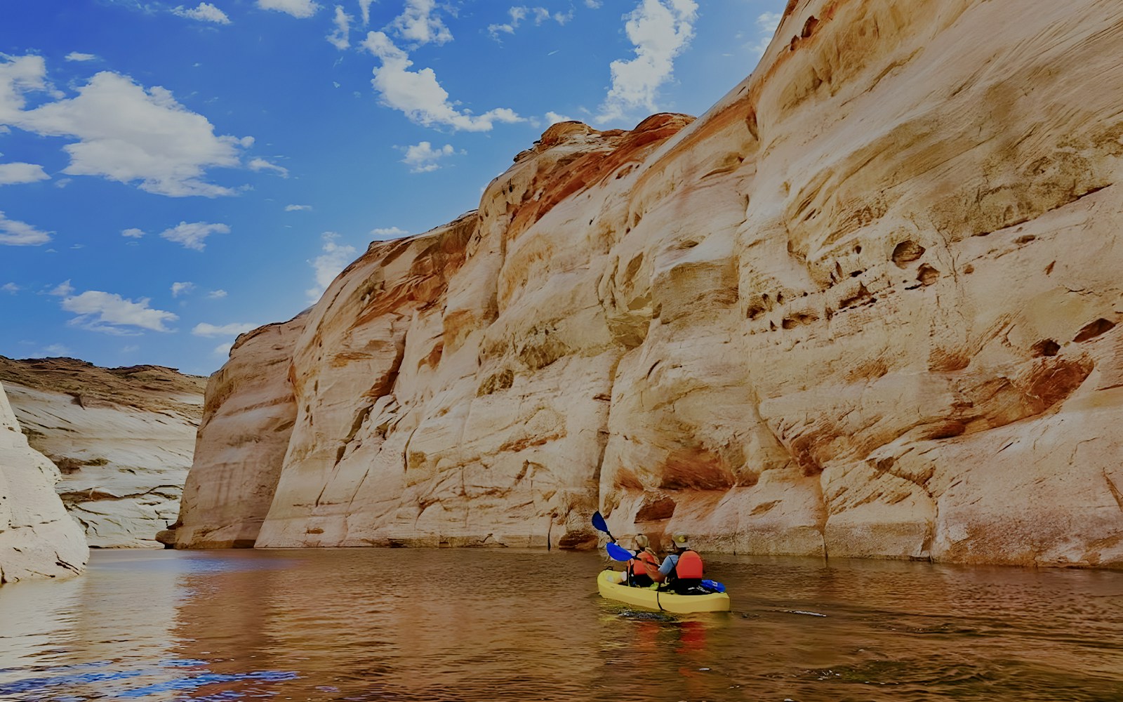 Kayakers paddling on Lake Powell near Antelope Canyon's sandstone cliffs.