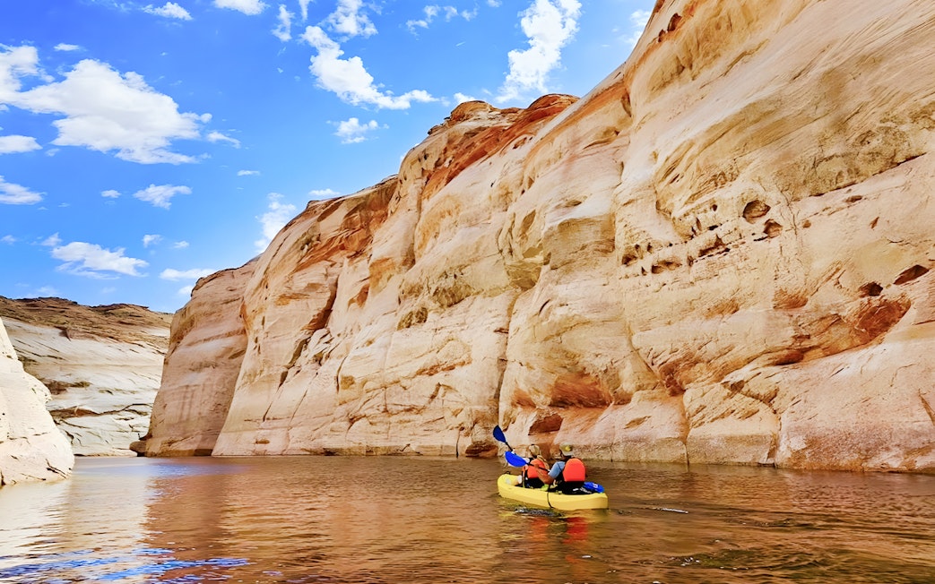 Kayakers paddling on Lake Powell near Antelope Canyon's sandstone cliffs.