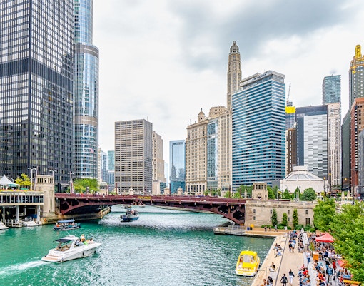 Chicago River Walk with boats near Michigan Avenue Bridge and city skyline.