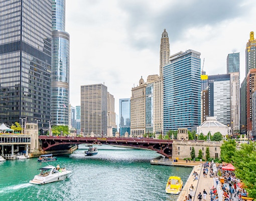 Chicago River Walk with boats near Michigan Avenue Bridge and city skyline.